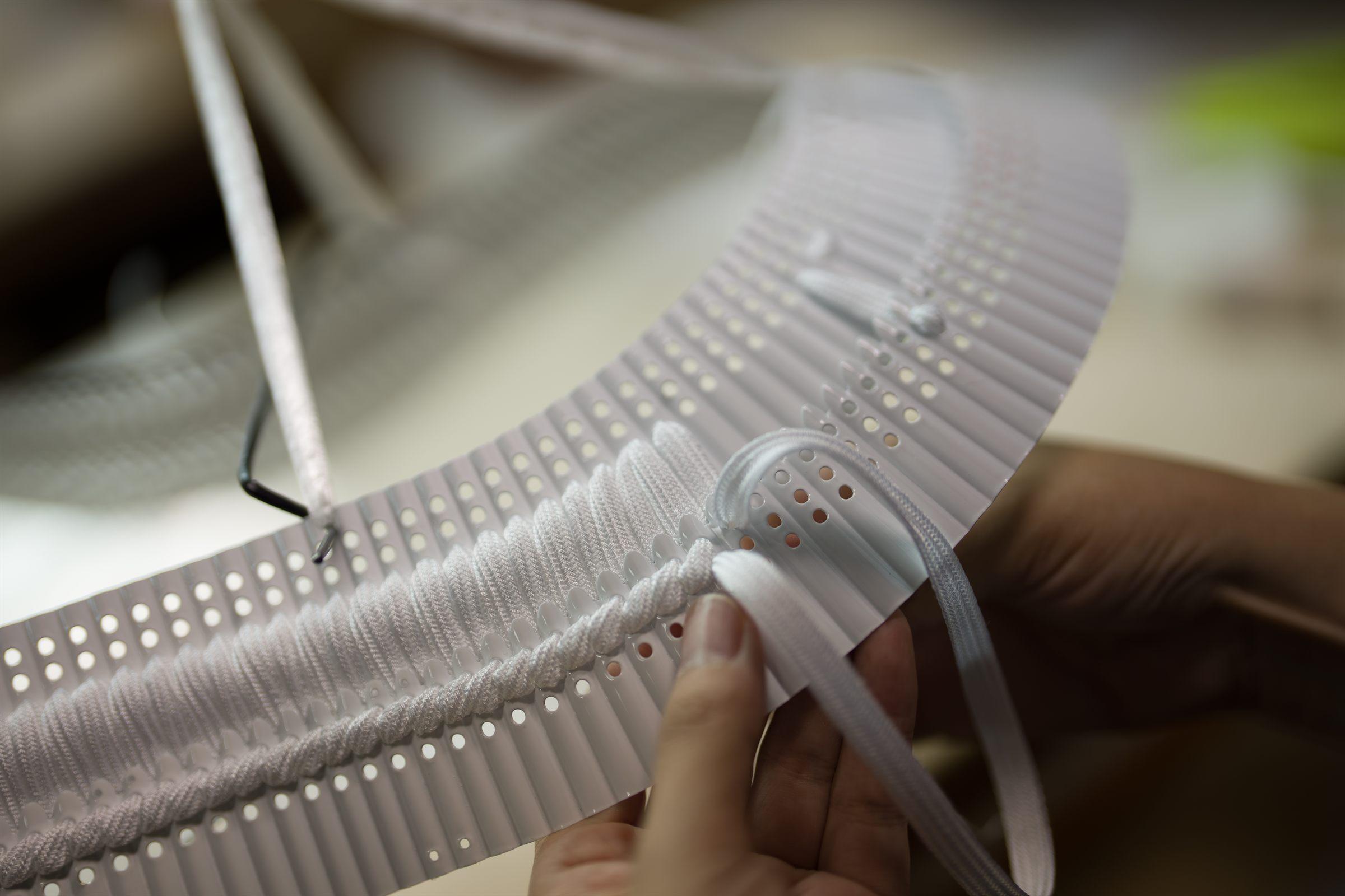 Hands lacing white silk cord through armour plates